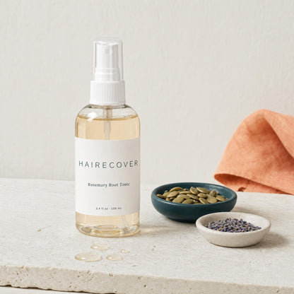 HAIRECOVER Rosemary Root Tonic bottle on stone with small dishes of pumpkin seeds and dried lavender buds
