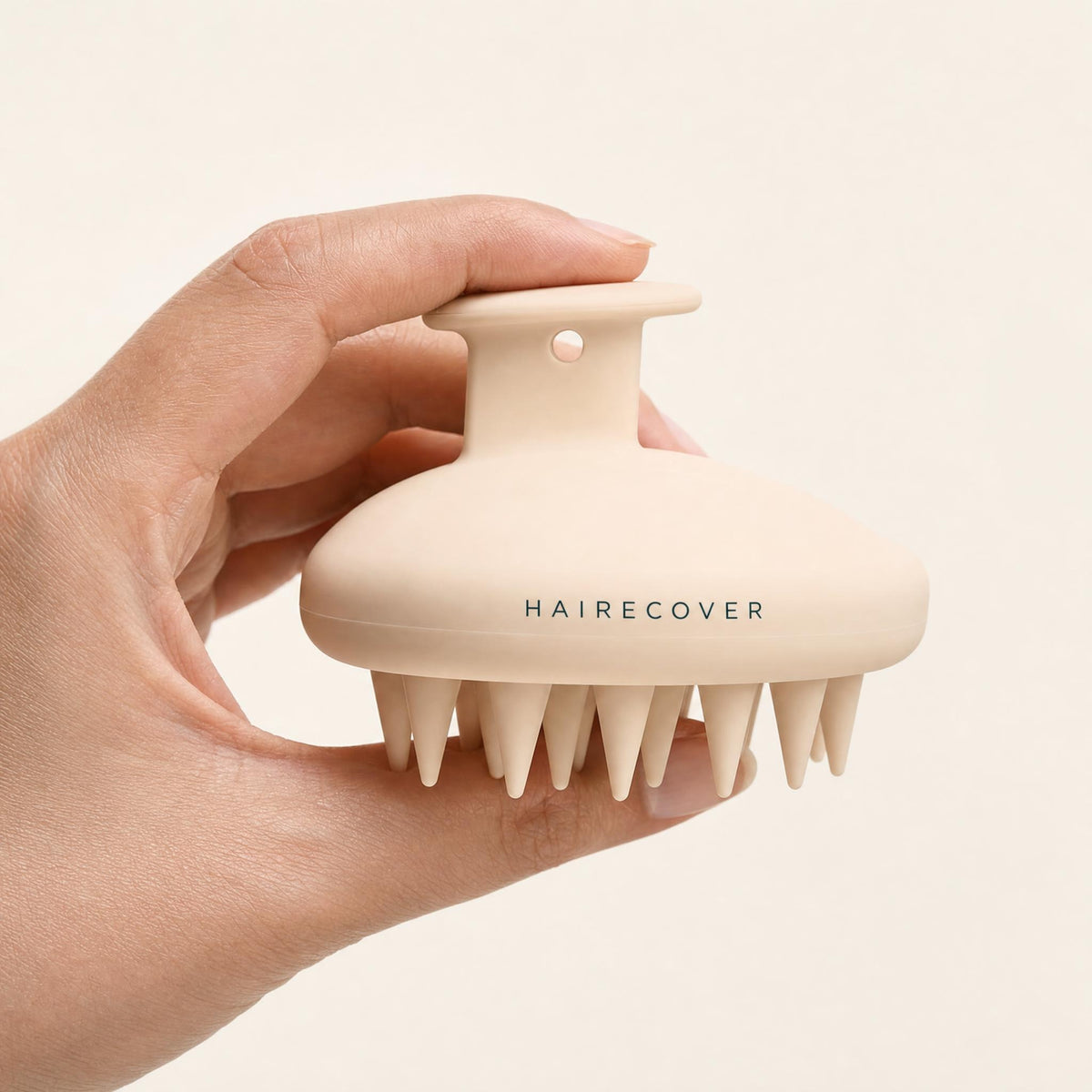 Hand holding the HAIRECOVER silicone scalp massager, side view of the knob grip and soft bristles