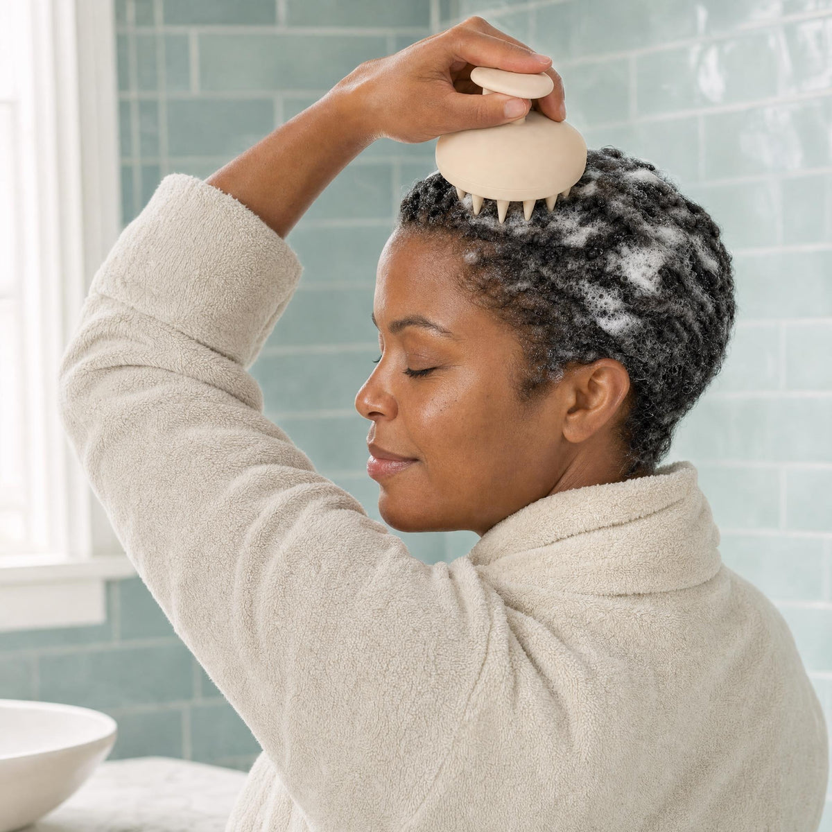 Woman massaging shampoo lather into her scalp with the HAIRECOVER silicone scalp massager at the bathroom sink