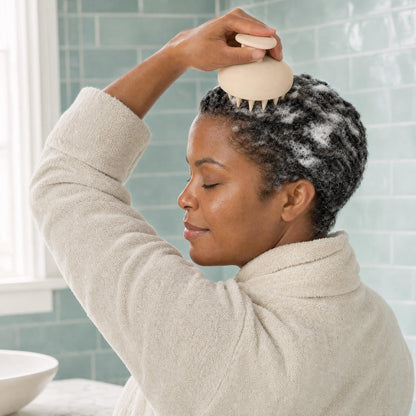 Woman massaging shampoo lather into her scalp with the HAIRECOVER silicone scalp massager at the bathroom sink