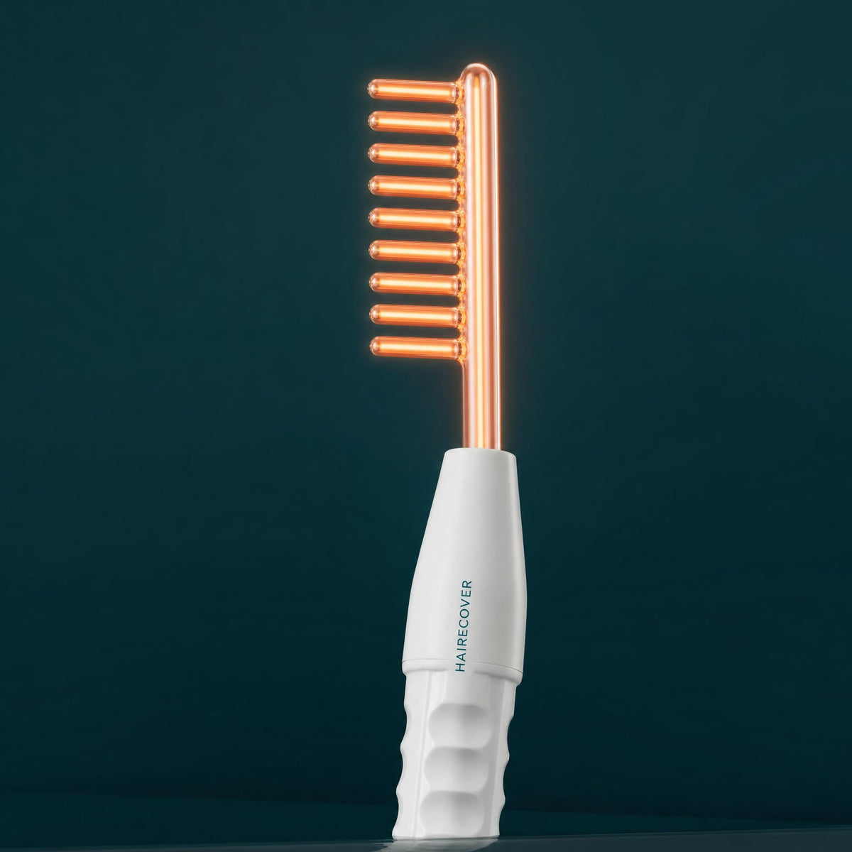 HAIRECOVER glass comb electrode attached to the GlowComb scalp wand, glowing soft orange-pink on a dark background